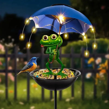 Decorative garden stake with a frog holding an umbrella and a bird, illuminated by fairy lights.
