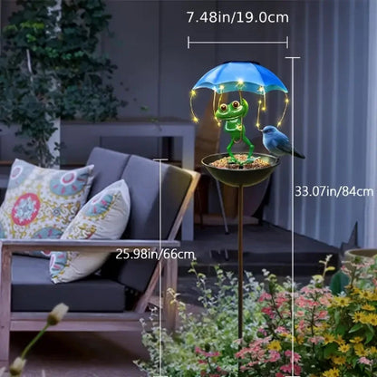 Decorative garden light with a frog holding an umbrella, bird, and flowers in a garden setting.