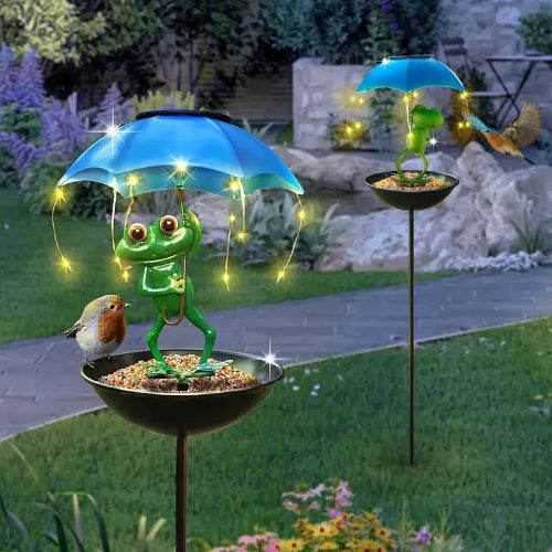 Decorative garden stake with a frog holding an umbrella, surrounded by lights in a garden setting.