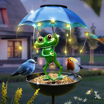 Decorative garden ornament with a frog holding an umbrella, birds, and lights in a backyard setting.